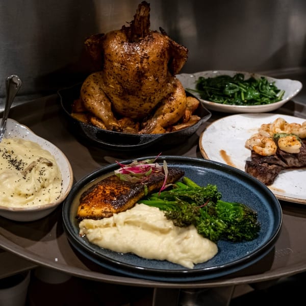 Tray with roasted chicken, steak and shrimp, fish, mashed potatoes, broccolini, and spinach.