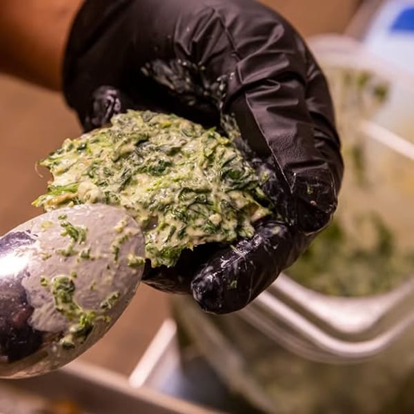 Chef's gloved hand holds a spoonful of creamy green spinach mixture.
