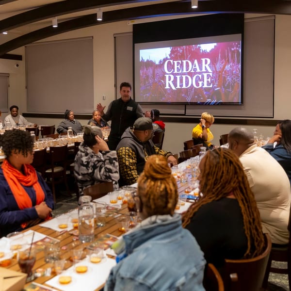 A man speaks to a group at tables with tasting glasses, "Cedar Ridge" projected on screen.
